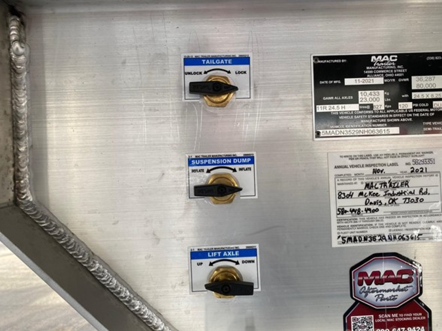 Mac Western trailer control panel area showing tailgate, suspension dump, and lift axle valves with labels and MAC tag in metal panel.
