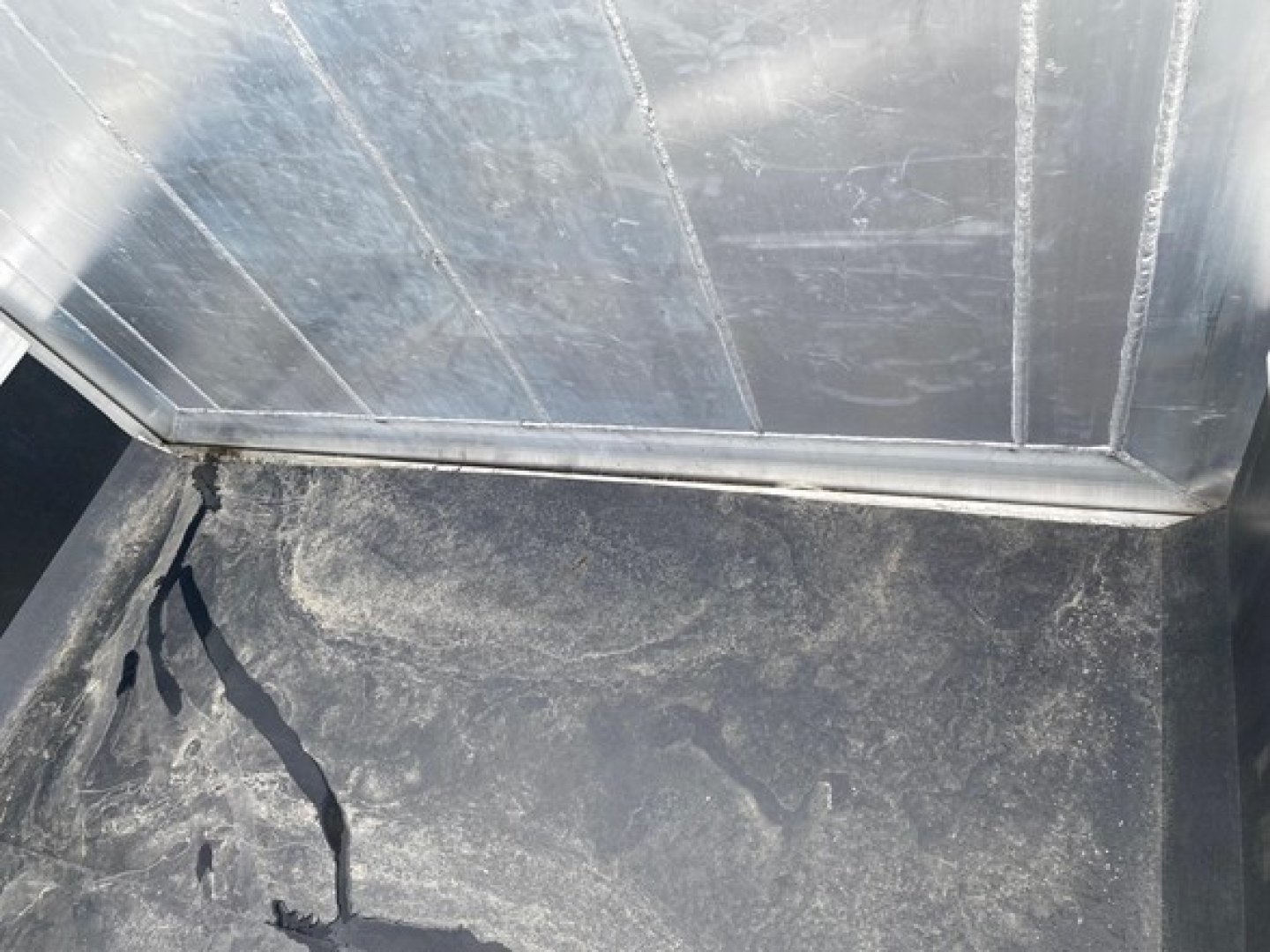 Trailer interior showing a cracked rubber floor mat and metal walls in a new dump trailer, with scuff marks and a damaged seam at base of side wall.