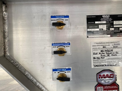 Tailgate, suspension dump, and lift axle control levers with labels; MAC Trailers data plate on the right; various stickers and controls on aluminum trailer wall.