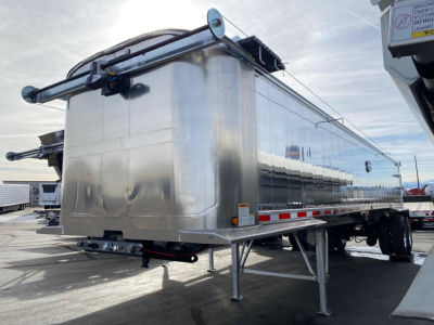 Trailer side and rear view of a new Mac Western lightweight aluminum end dump trailer showing polished aluminum body, rear hinge, and support legs.