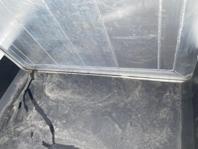 Trailer interior showing a cracked rubber floor mat and metal walls in a new dump trailer, with scuff marks and a damaged seam at base of side wall.