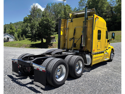 Peterbilt 579 UltraCab tractor in yellow, rear view showing fifth wheel, dual rear axles, and three axle setup with chrome wheels.
