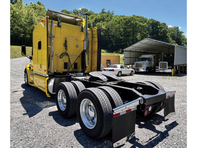 Peterbilt 579 UltraCab truck chassis with yellow sleeper cab, dual rear axles, and flatbed undercarriage in outdoor lot.