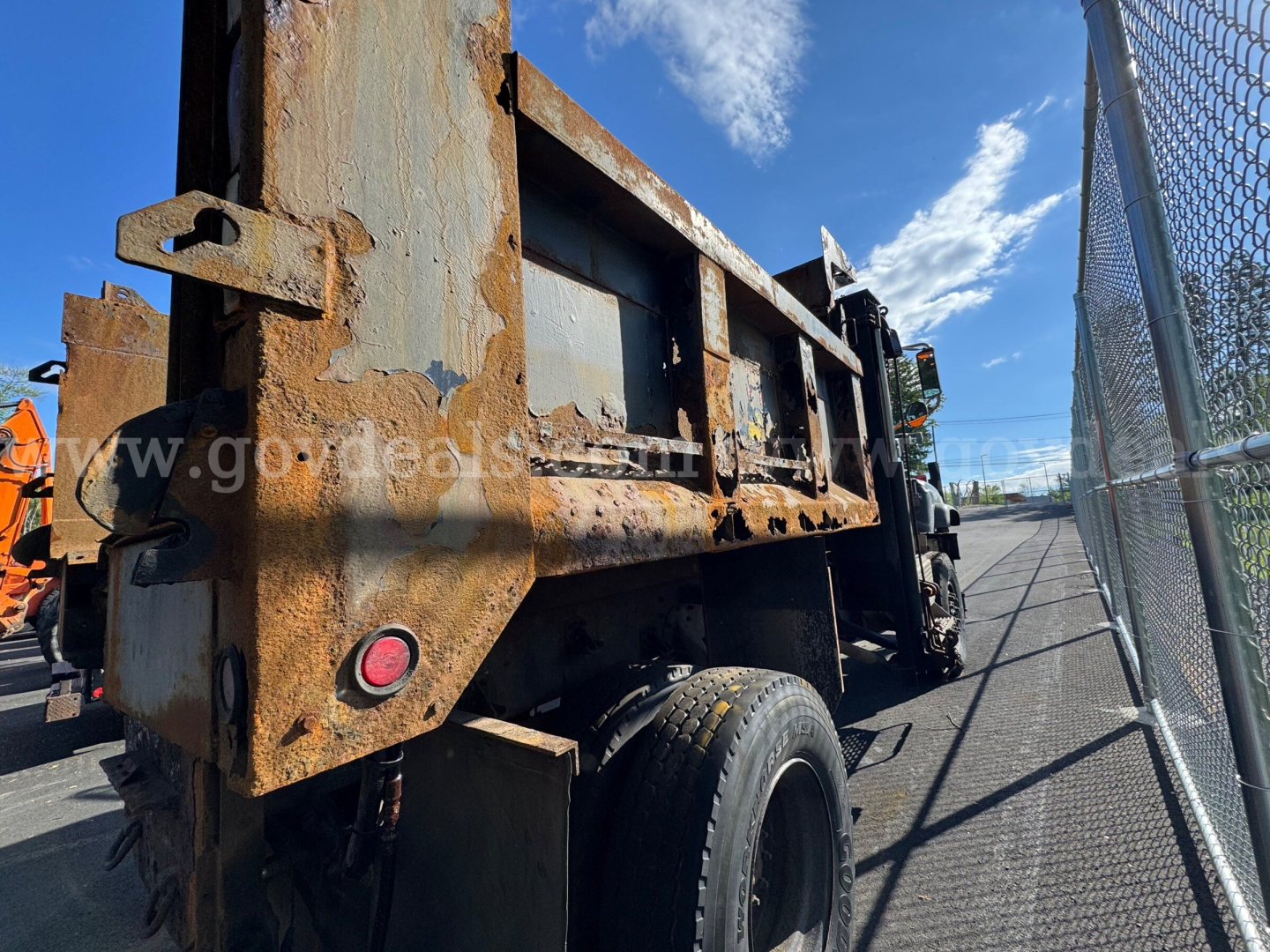Truck dump bed side view showing rusted steel containment and rear wheel, International 5600i dump truck, rusted metal surface, clear blue sky.