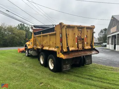 Dump truck with plow and wing, rear view showing yellow dump body and tri-axle wheels.