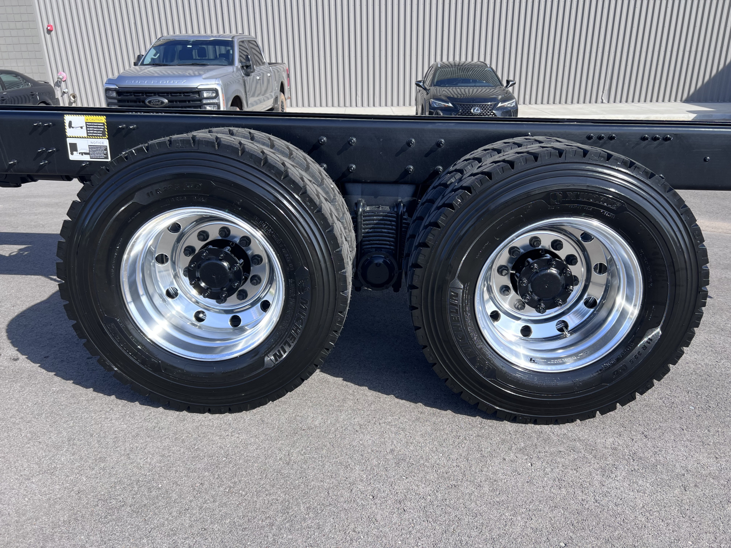 Twin rear axles with polished wheels and heavy-duty tires on a Mack GR64B chassis showing wheels and suspension components.