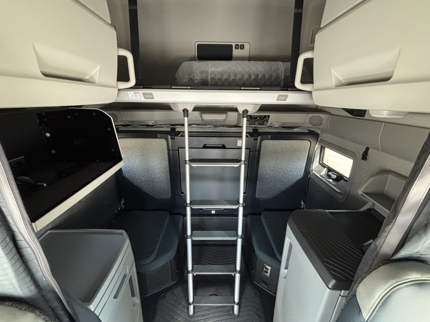 Cab interior of a Volvo VNL64T860 tractor unit showing a vertical ladder and sleeper area with storage compartments and window on right side.