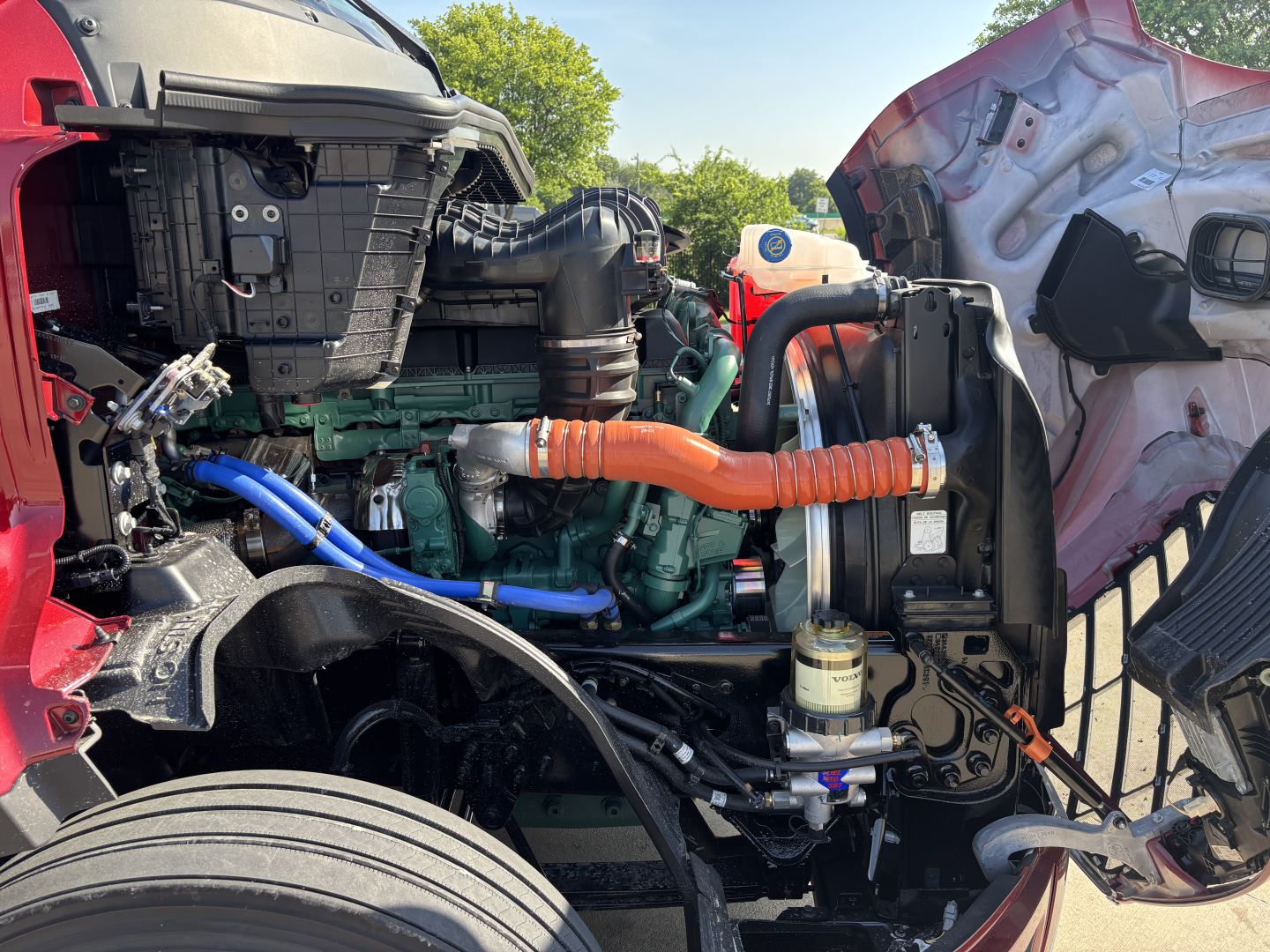 Volvo VNL64T860 engine bay with orange turbo intercooler hoses, blue coolant hose, green engine block, and various black plastic components visible.