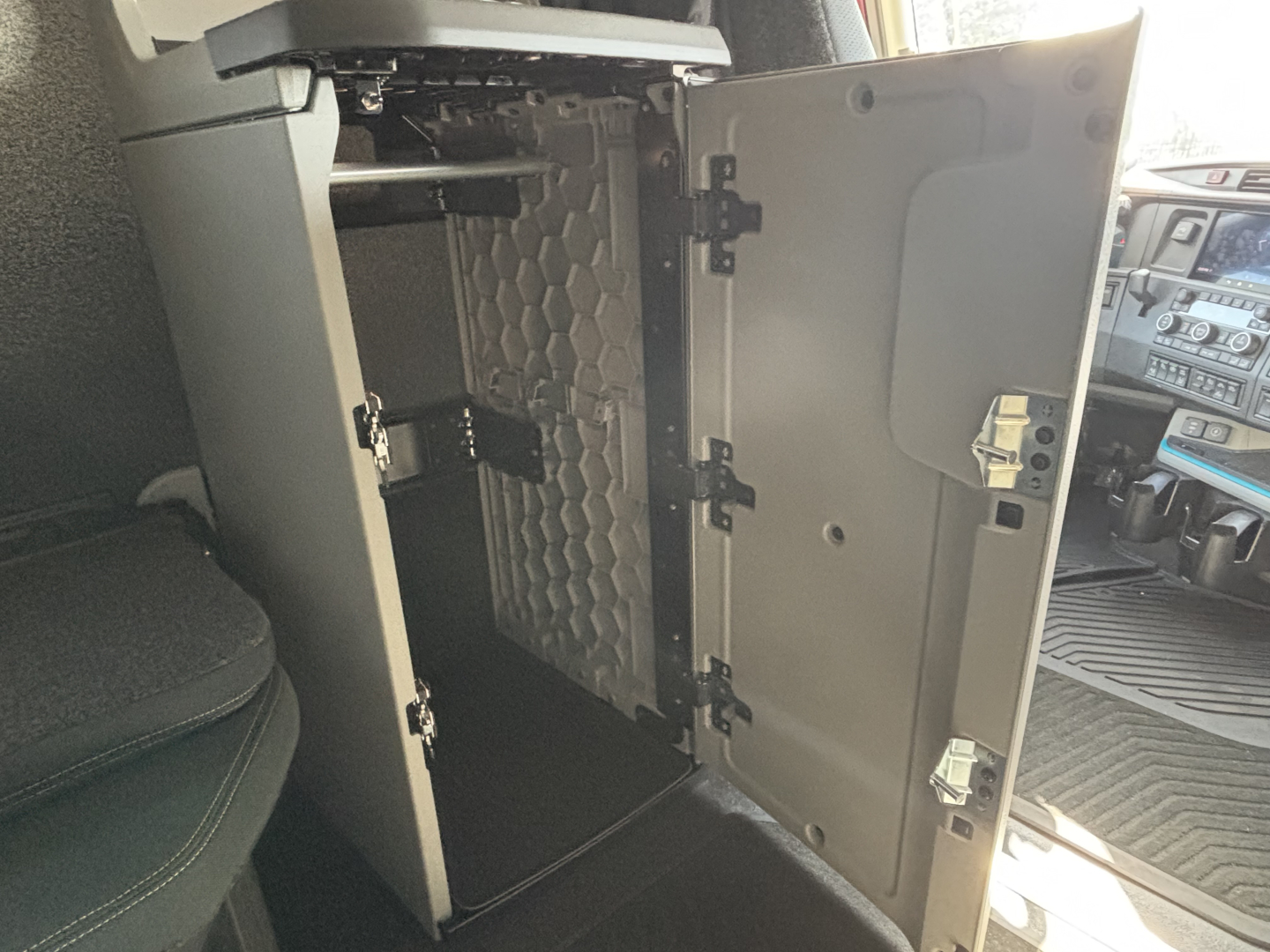 Volvo VNL truck cab interior showing open storage cabinet behind the driver seat with shelves and latching hinges.