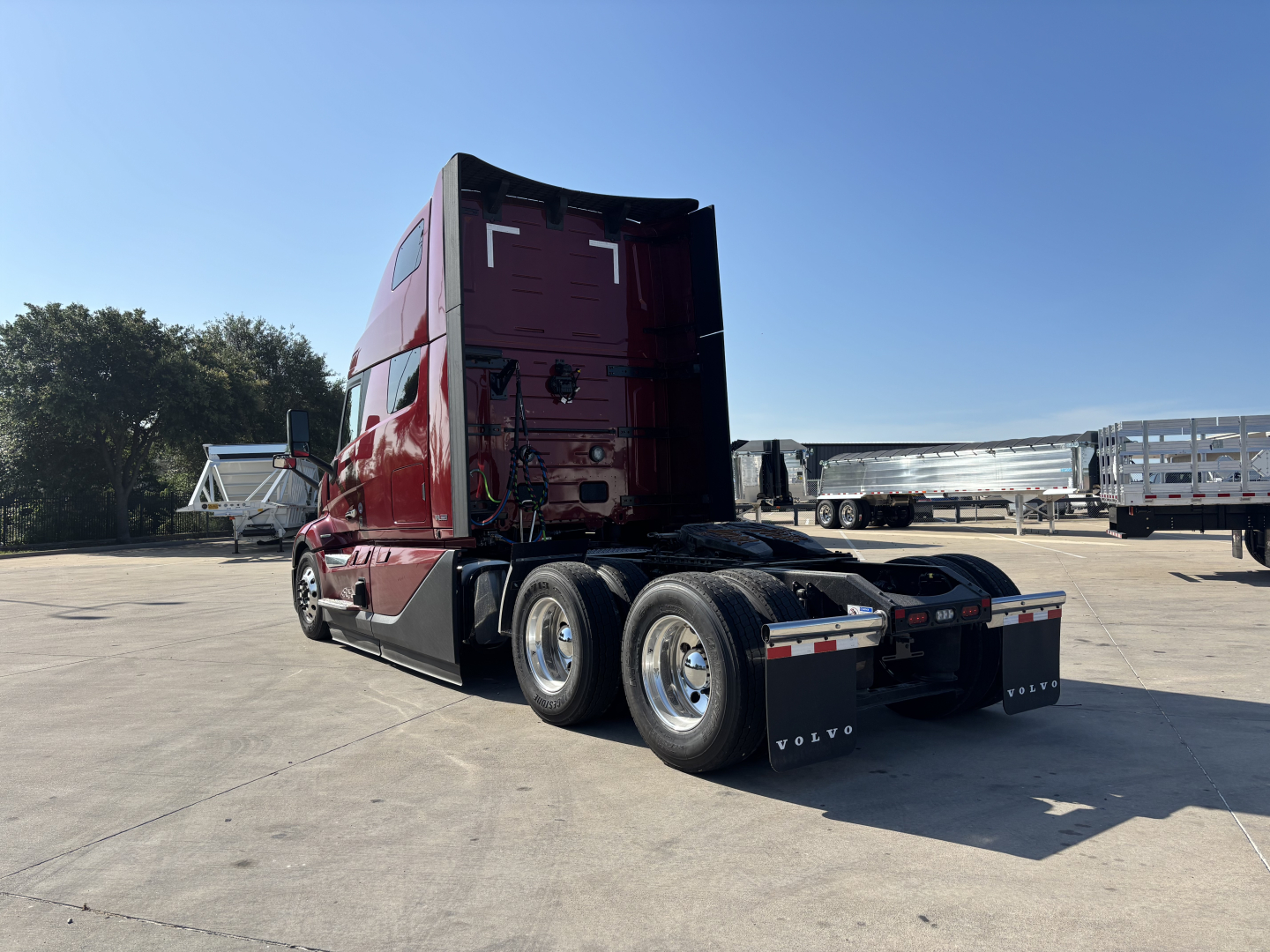 Volvo VNL64T860 sleeper cab semi-truck rear-right view showing red cab, dual rear axles, and fifth wheel; Volvo mudflaps and wheel rims visible.