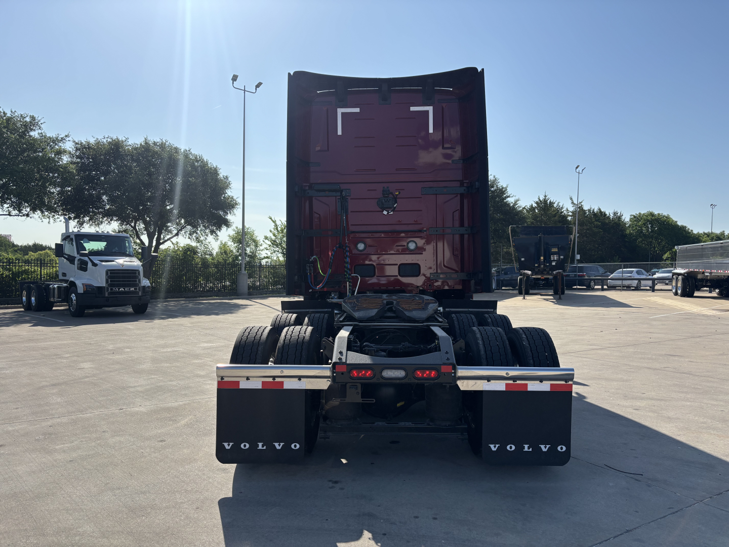 Volvo VNL64T860 truck rear view showing fifth wheel, dual rear axles, mud flaps with VOLVO text, and red sleeper cab in a dealership lot.