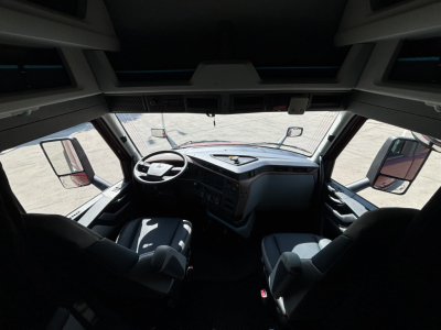 Volvo truck cab interior view from the sleeper hood area showing steering wheel, driver and passenger seats, dashboard, and mirrors.