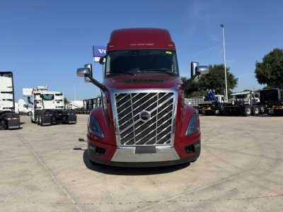 Front view of a red 2027 Volvo VNL64T860 truck with large chrome grille and Volvo emblem, daytime dealership lot.