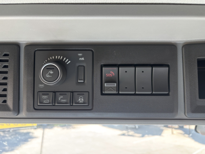 Truck instrument panel with control knobs and warning buttons, including circular knob, several rectangular switches, and a red SOS button.