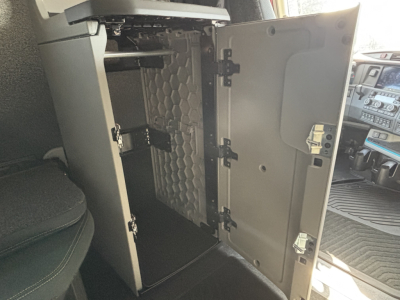 Volvo VNL truck cab interior showing open storage cabinet behind the driver seat with shelves and latching hinges.