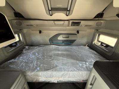Volvo VNL64T860 sleeper cab interior with bed protected by plastic, overhead storage, and side windows visible.