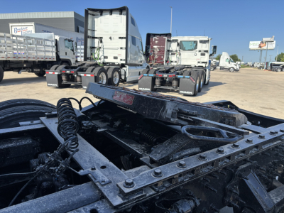 Truck chassis in a dealership lot showing the rear frame and fifth wheel area of a new Volvo VNL model with multiple trucks in background.