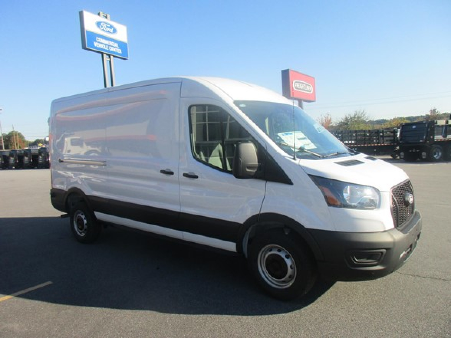 Ford Transit cargo van in a dealership lot showing side and front view with white body and black bumper, windows, and wheels.