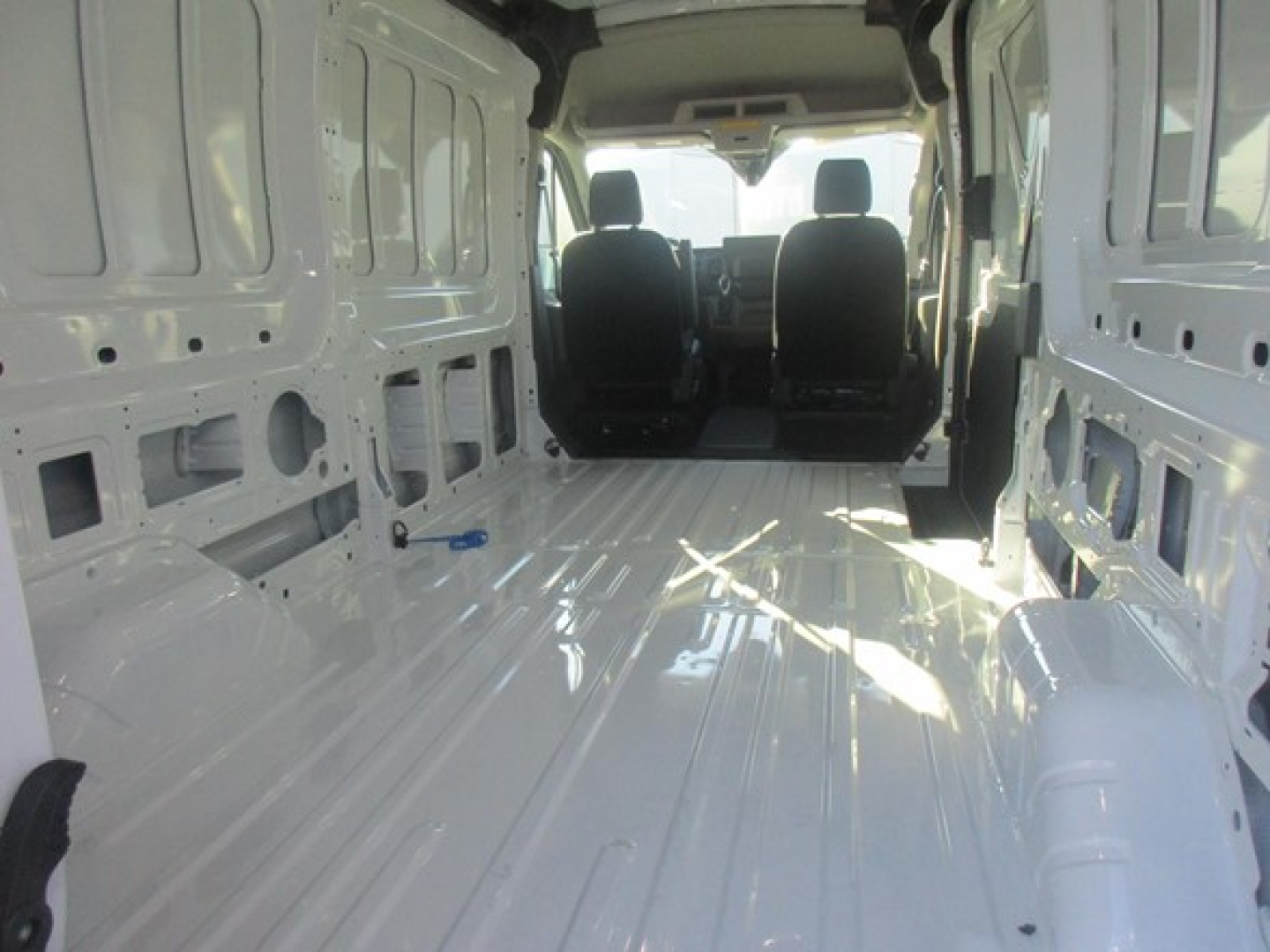 Ford Transit cargo van interior view showing bare metal cargo area with ribbed floor, sidewall panels, and two front seats; no branding text visible inside.