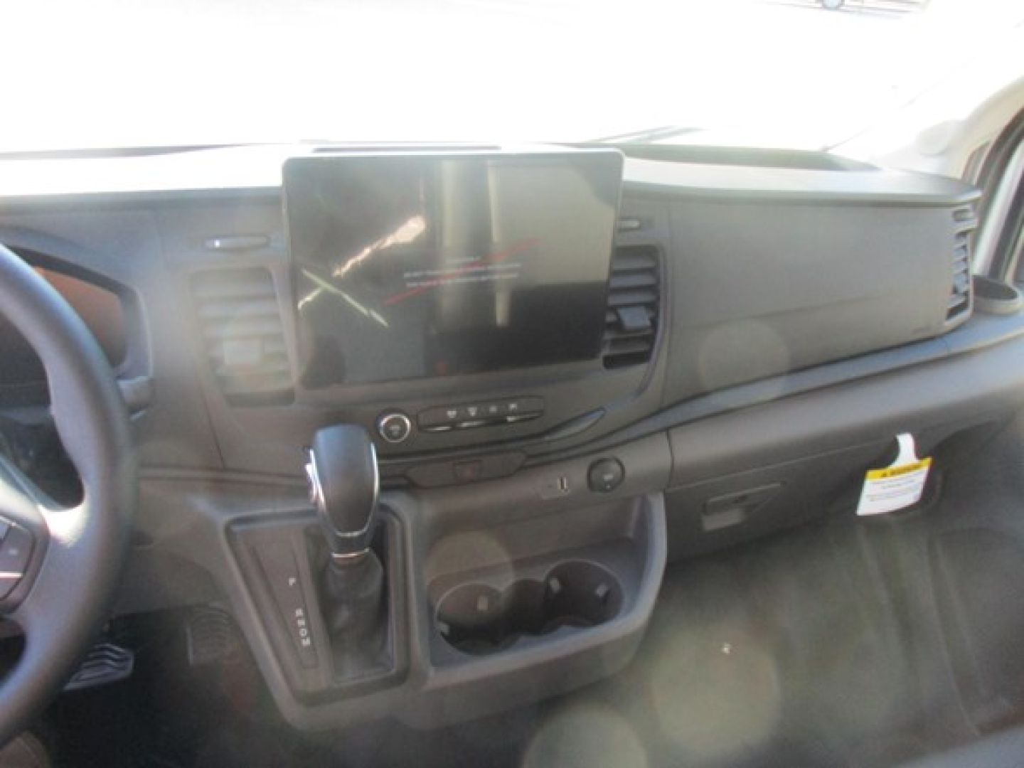 Ford Transit cargo van interior showing center infotainment screen, steering wheel, gear shifter, and dashboard controls.