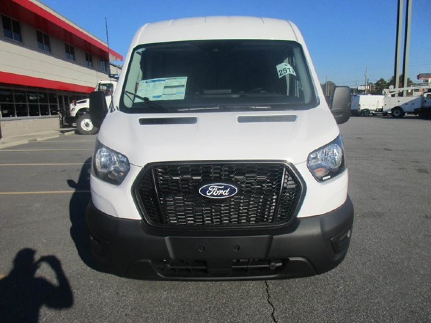 Front view of a white 2026 Ford Transit cargo van showing Ford emblem grille and windshield with dealer stickers.