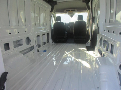 Ford Transit cargo van interior view showing bare metal cargo area with ribbed floor, sidewall panels, and two front seats; no branding text visible inside.