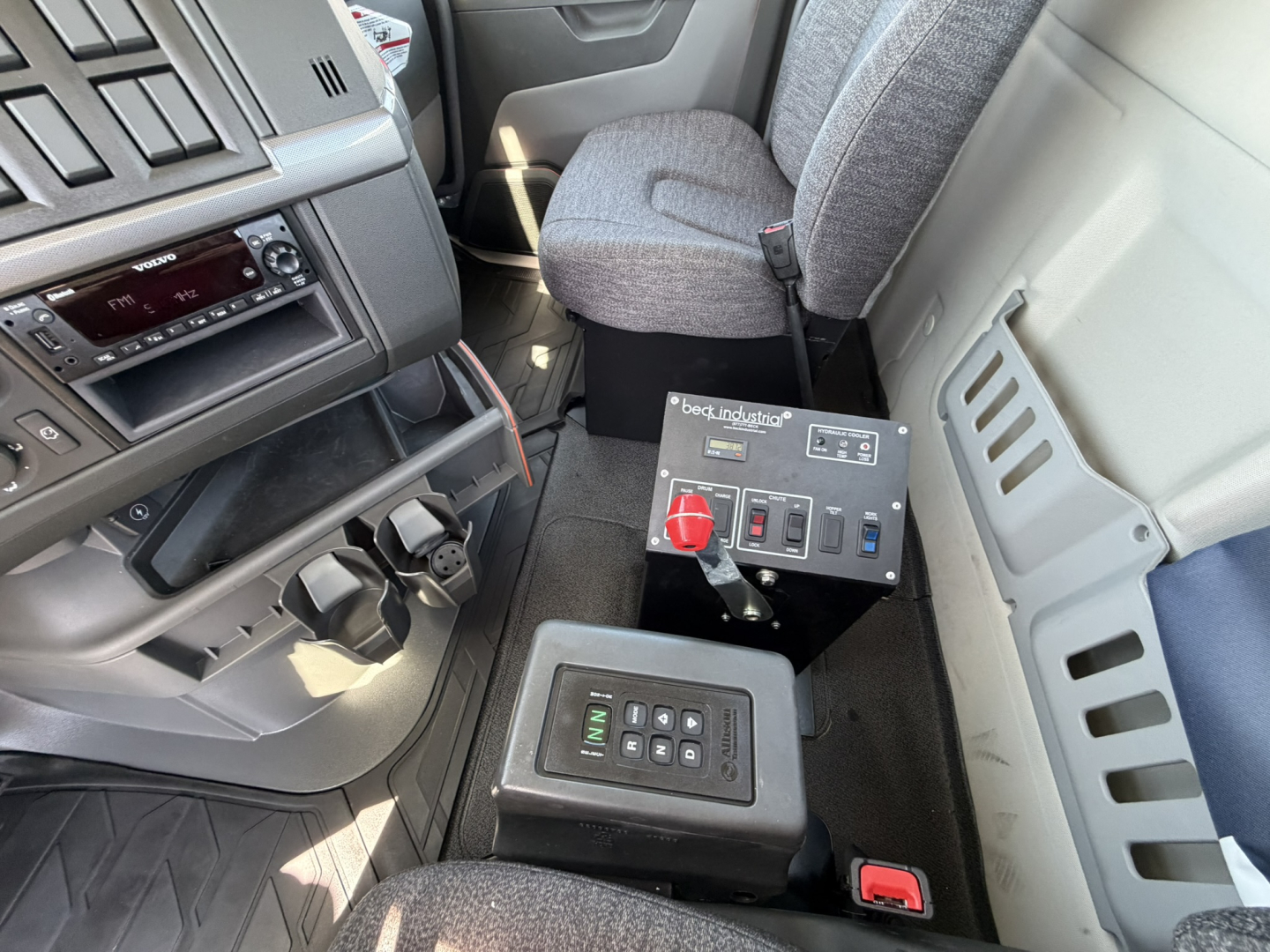 Volvo VHD64B300 mixer truck interior showing dashboard, center console, gear selector, and auxiliary control panel with red emergency stop and switches.