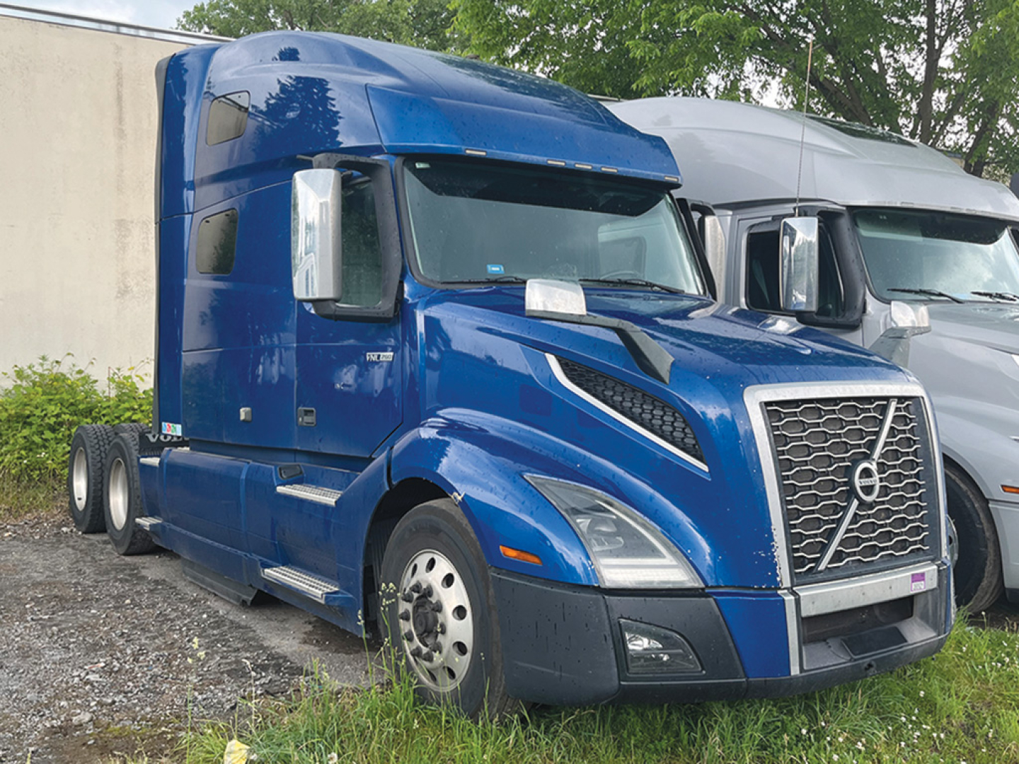 Truck cab showing blue Volvo VNL 760 sleeper with large grille and chrome mirrors, front view, two axles visible, day-time outdoor lot.