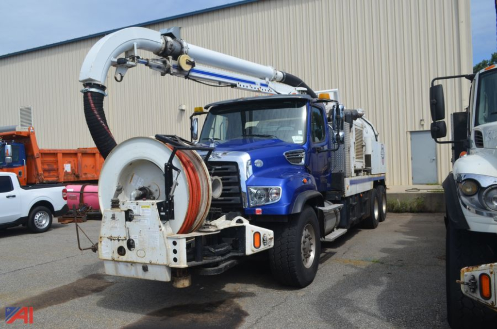 Vacuum truck with large hose reel and boom mount on a Freightliner chassis, blue cab, in-service equipment showing hose reel and piping components.