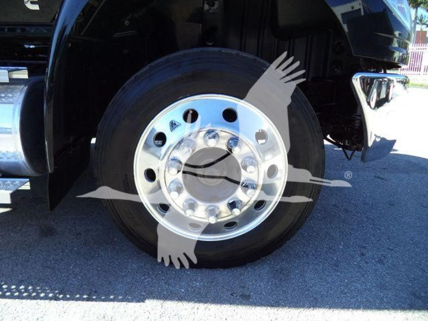Wheel and front tire on a 2022 International MV rollback truck showing polished aluminum wheel and hub, with fender and bumper in view.
