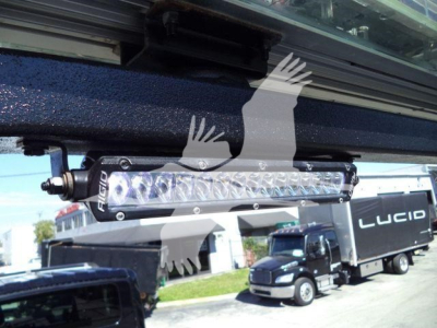 Truck recovery light bar mounted under the cab with visible bolts and LED strip, International MV truck in background.