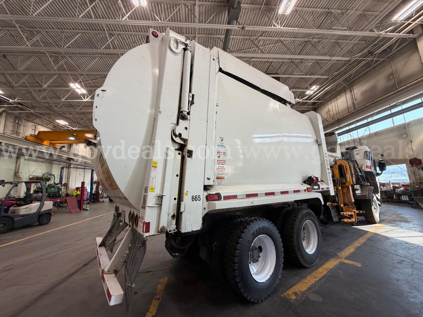 Waste/garbage truck rear view showing large cylindrical body and dual rear axles with white paint.