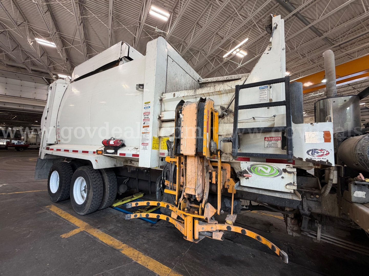 Peterbilt 520 garbage truck side view showing rear compactor and hydraulic lift system with yellow arms.