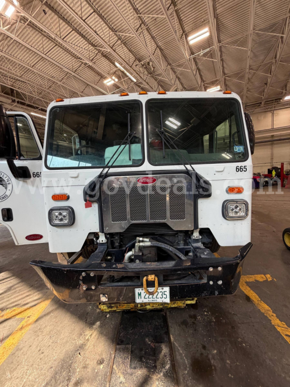 Peterbilt 520 garbage truck front view with grille, windshield, and bumper in a warehouse setting.