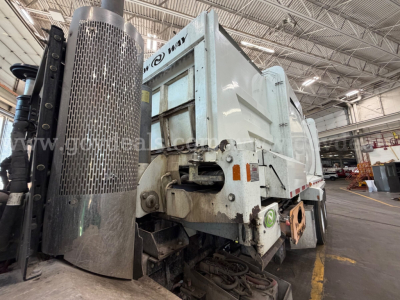 Peterbilt 520 dump truck in an indoor facility showing rear side with hydraulic components and exhaust stack.