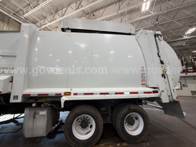 Peterbilt 520 rear side view garbage truck showing large waste body with dual rear wheels and load hopper inside a warehouse.