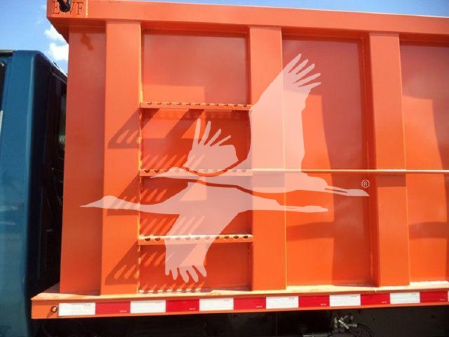 Dump truck dump body with orange exterior and ladders on side, International MV branding visible