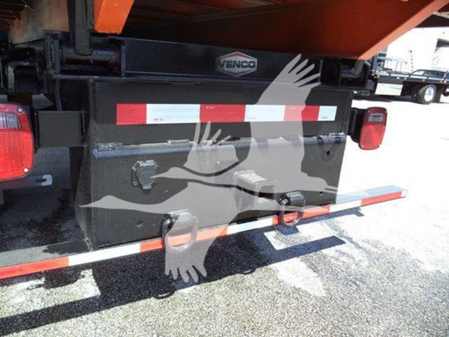 Dump truck rear showing storage toolbox with Venco label and reflective red/white bars.