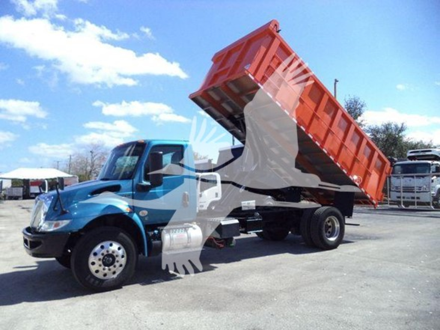 Dump truck with raised red dump bed on a blue International MV truck. Side mirrors, fuel tank, and dual rear wheels visible.