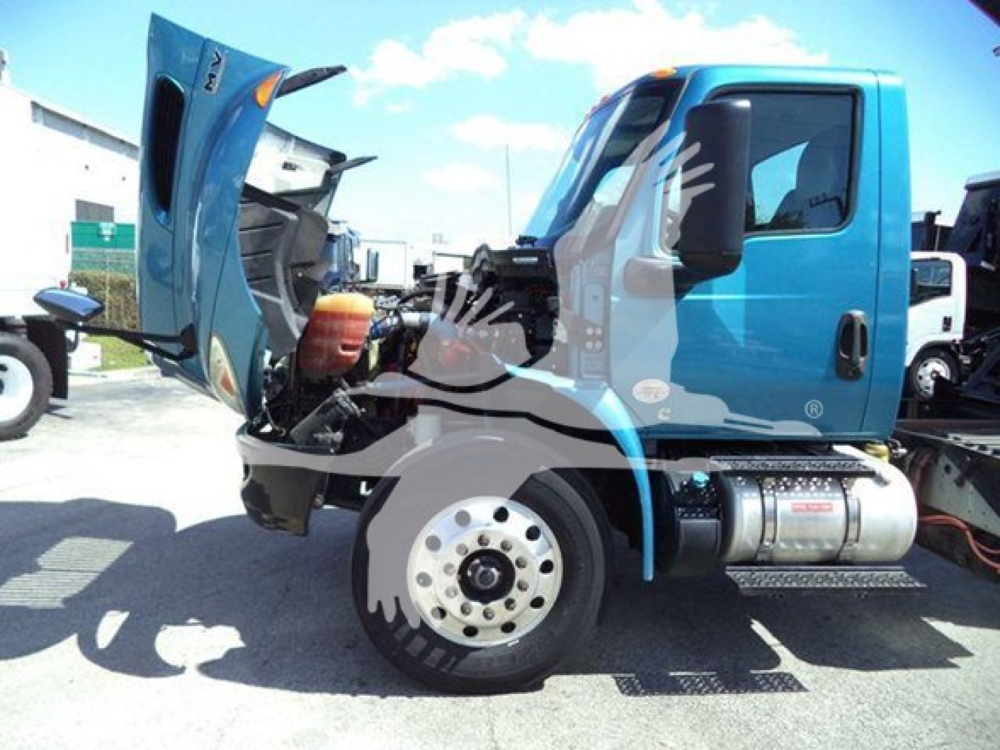 Truck cab with hood open, showing engine bay and chassis on a blue International MV dump truck, front wheel visible, side view with water bottle and step area.