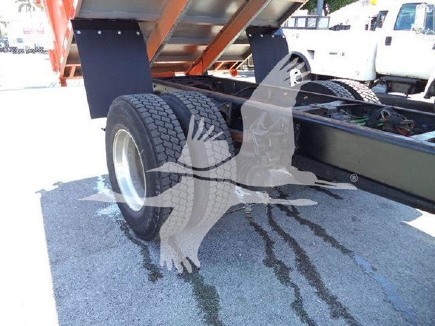 Truck rear axle area of a 2020 International MV dump truck showing dual rear wheels and chassis with hydraulic lines; part of dump body elevated.