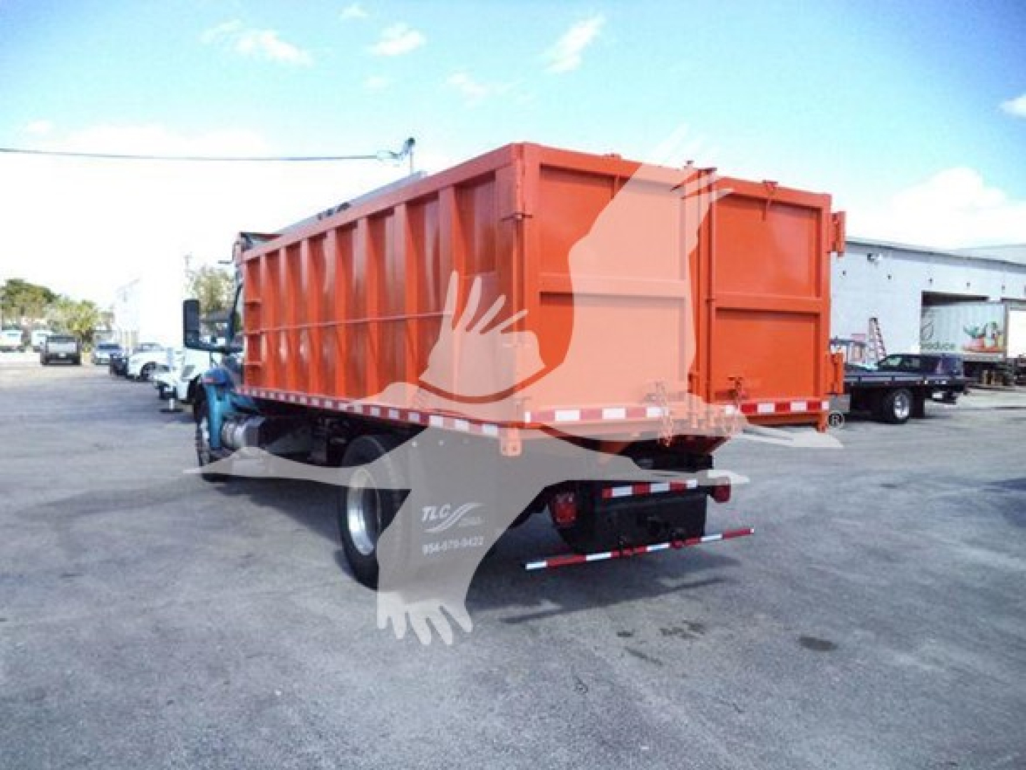 Truck dump bed rear view with orange dumpster-style dump body on a blue tractor; visible text on rear bumper area and sticker.