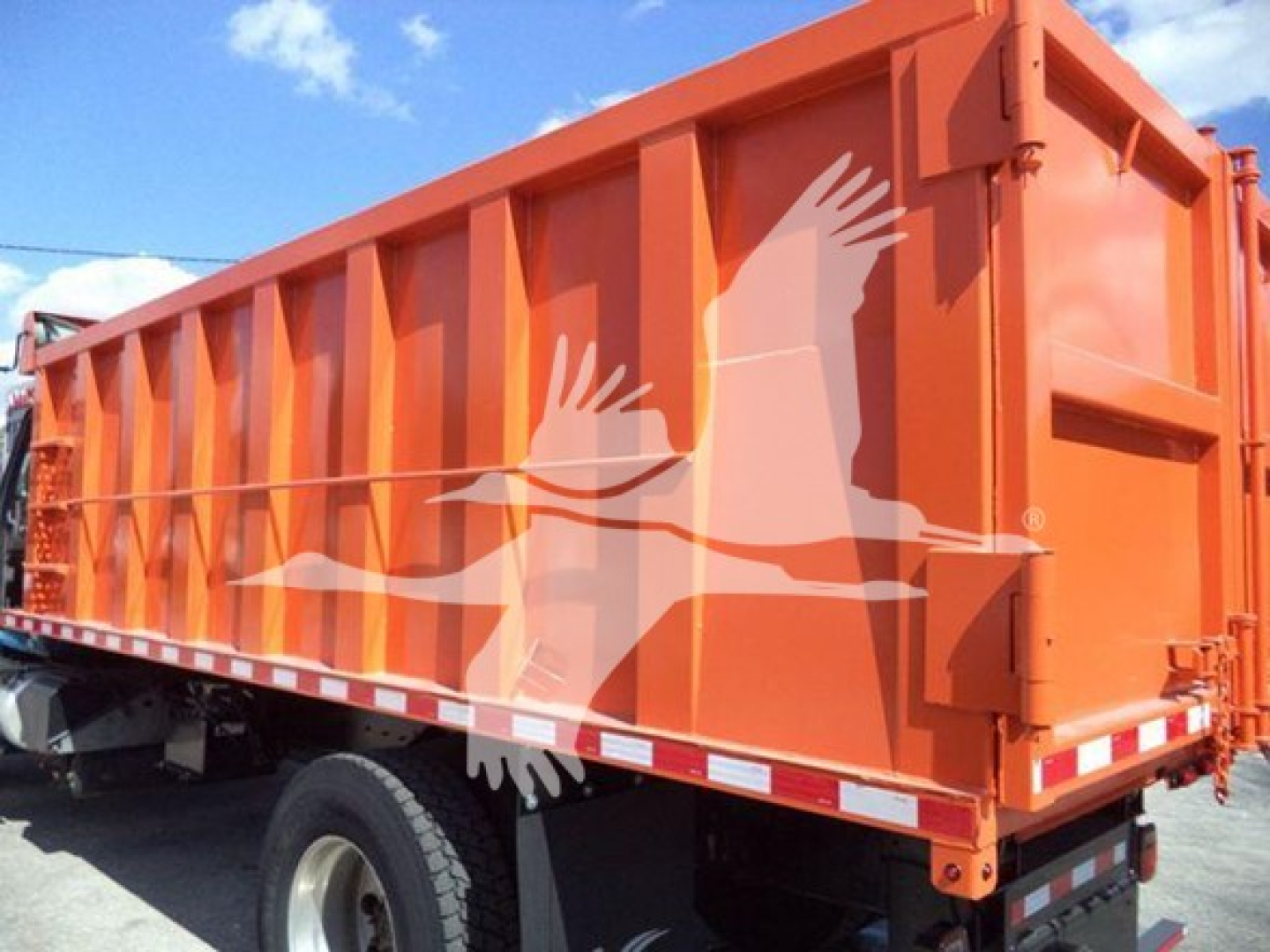 Dump truck side view showing orange dump bed with white bird logo and wheel/tire undercarriage.