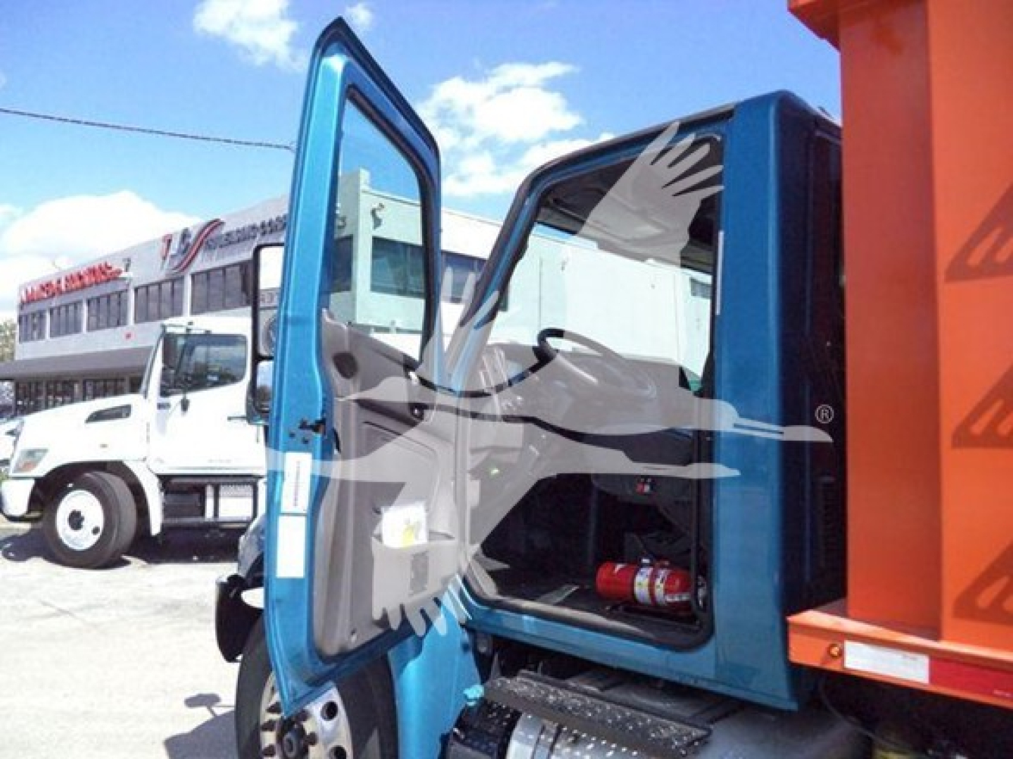 Truck cab door open showing interior, blue exterior with white interior, part of a dump truck with an orange container attached.