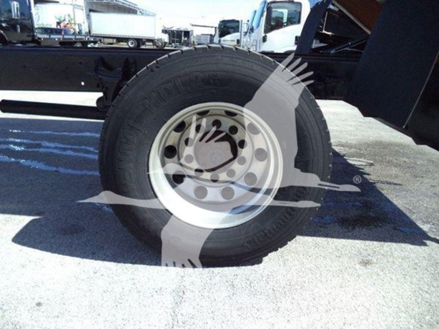 Trailer wheel and tire assembly shown under a dump truck chassis with rim and tire tread visible.