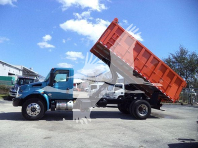 Truck side view showing a 2020 International MV dump truck with the dump bed raised, blue cab, red cargo bed, wheelbase, and surrounding lot.