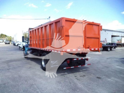Truck dump bed rear view with orange dumpster-style dump body on a blue tractor; visible text on rear bumper area and sticker.