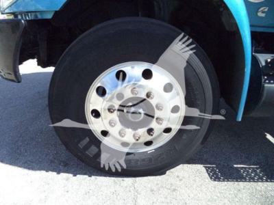 Truck wheel and tire on a blue International MV dump truck showing aluminum chrome dual-layer hub with lug nuts and tire sidewall reading 'BRIDGESTONE' and model details.