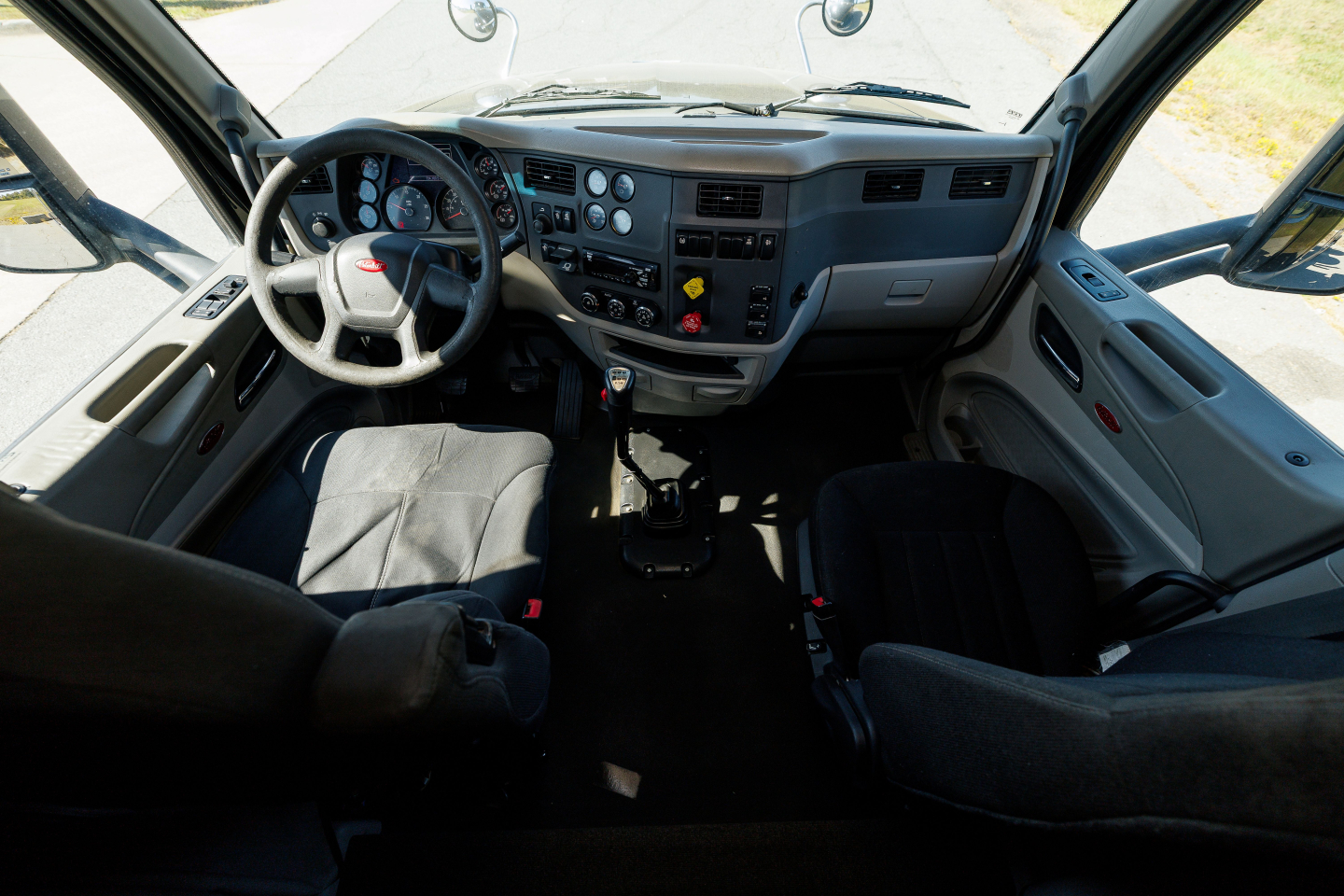 Truck cab interior showing steering wheel, dashboard, and seats from the driver’s side of a Peterbilt 579. Visible gauges, center console, and door panels.