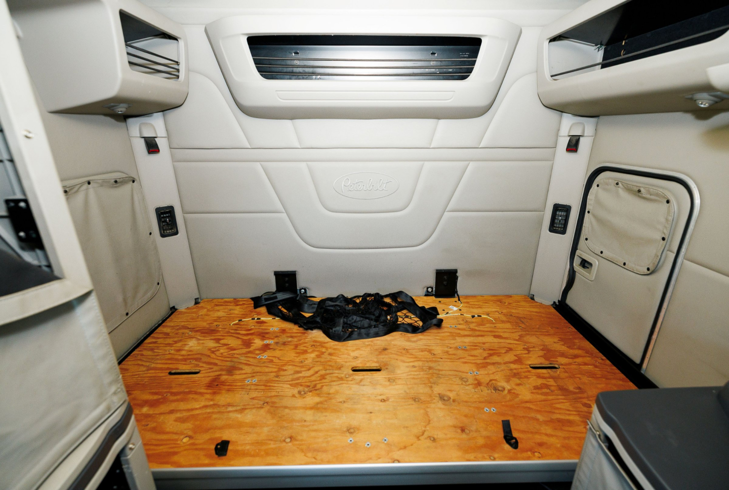 Peterbilt 579 sleeper cab interior cargo area showing bare plywood floor and side storage panels.